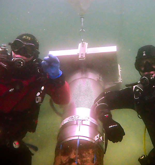 Deux plongeurs sous-marins en combinaison, l'un en rouge et l'autre en noir, posent à côté d'une crépine munie d'un pilote conçu par Dreissena Systems